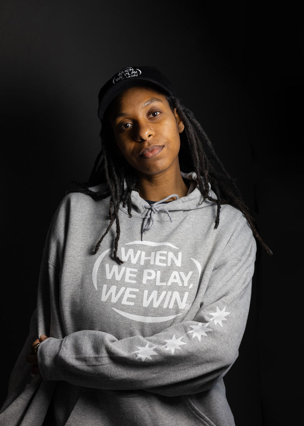 Person wearing a gray hoodie with 'When We Play, We Win' text on a black background