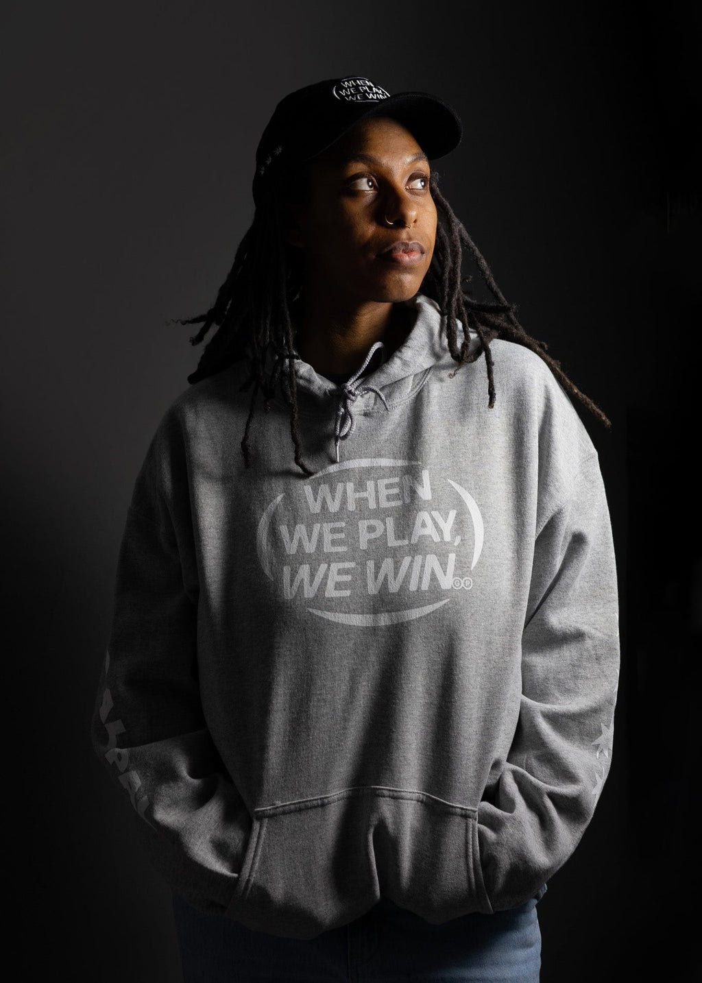 Person wearing a hoodie with 'When We Play, We Win' text on a dark background